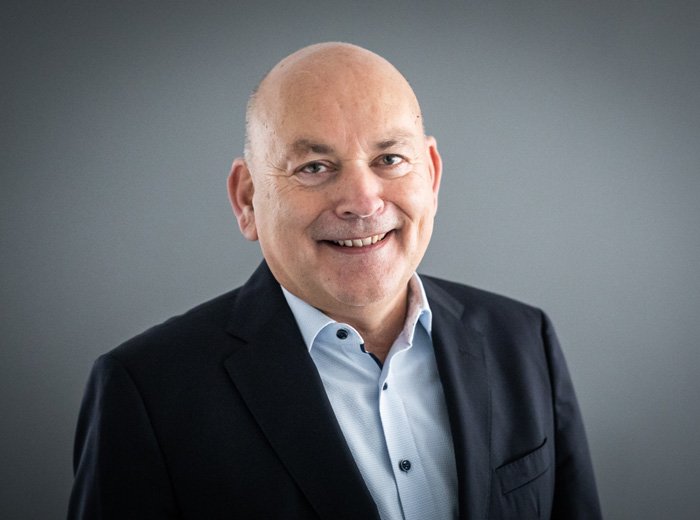 Porträt eines lächelnden, glatzköpfigen Mannes, Kay Nernheim, in einem dunklen Anzug mit hellem Hemd. Er blickt direkt in die Kamera und wirkt freundlich und professionell.